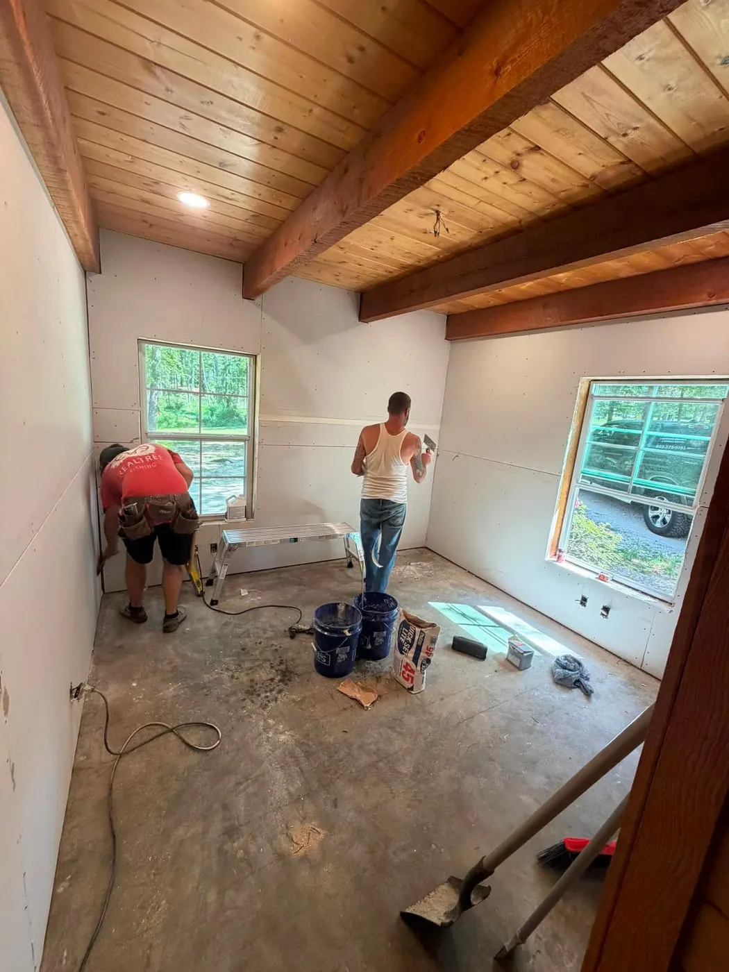 TrueCraft crew finishing drywall in a room with exposed wood beams