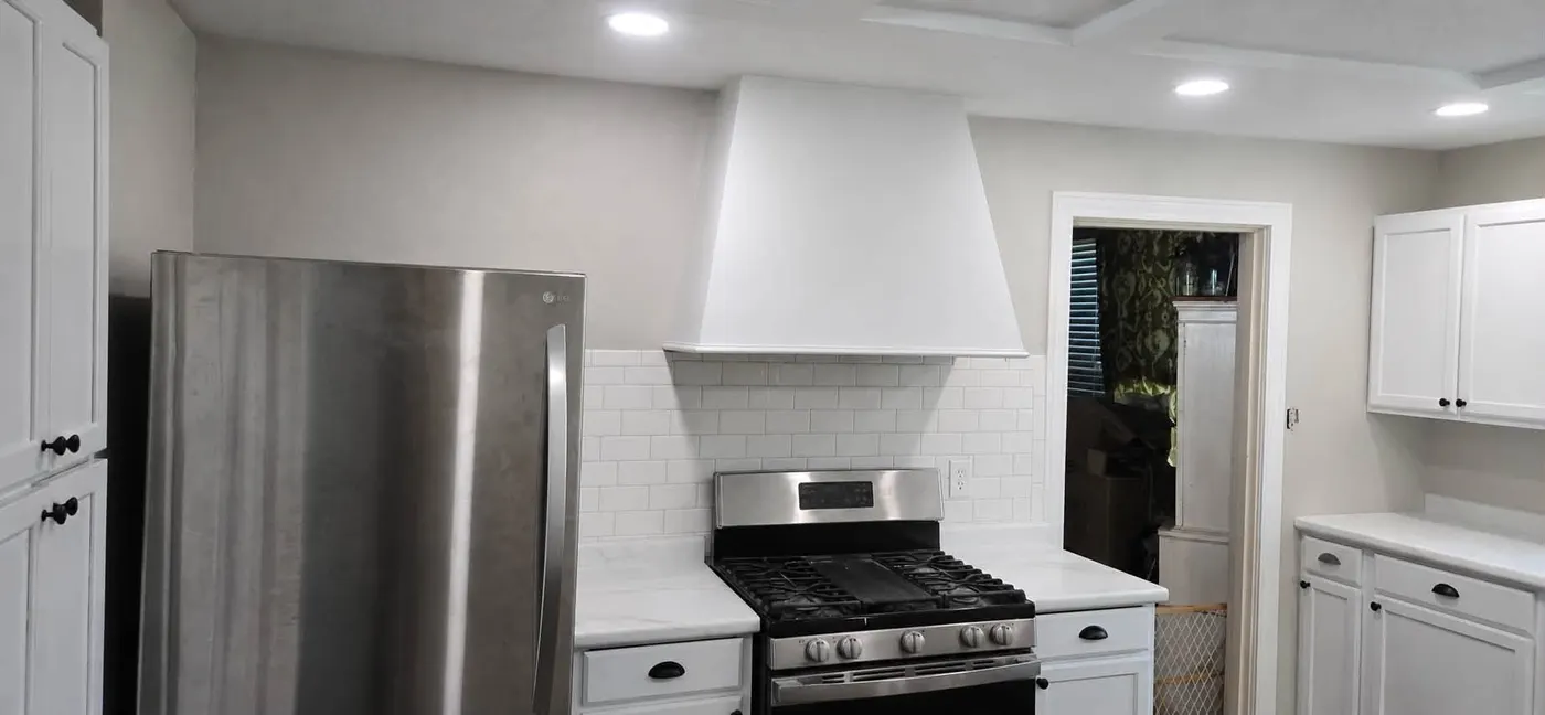 Remodeled kitchen with white shaker cabinets, marble-look counters, subway tile backsplash, and a custom white range hood