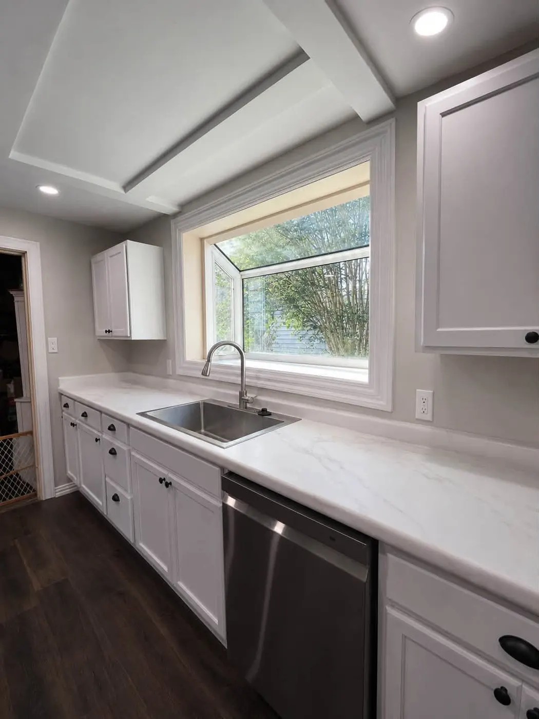 Remodeled kitchen sink wall with a new stainless sink, garden window, and white cabinets